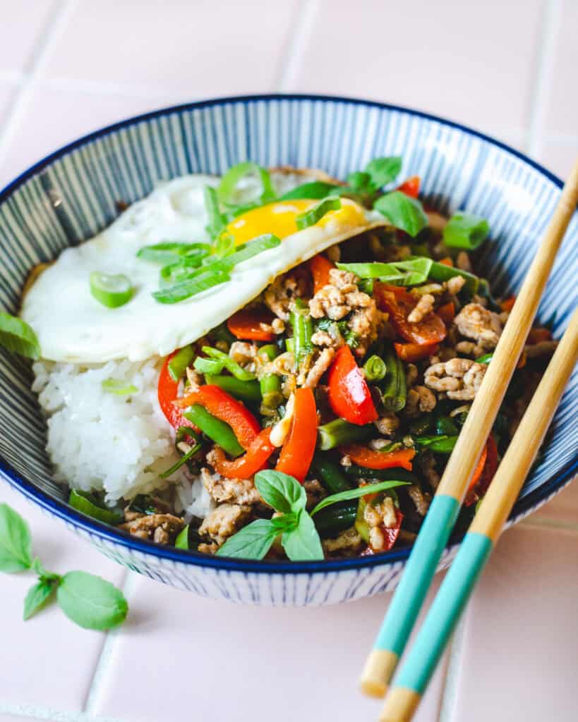 Pad krapow - Thai basilikum stir fry med svinekød og ekstra grøntsager. Lækker asiatisk aftensmad, serveret i en smuk skål med blå striber.