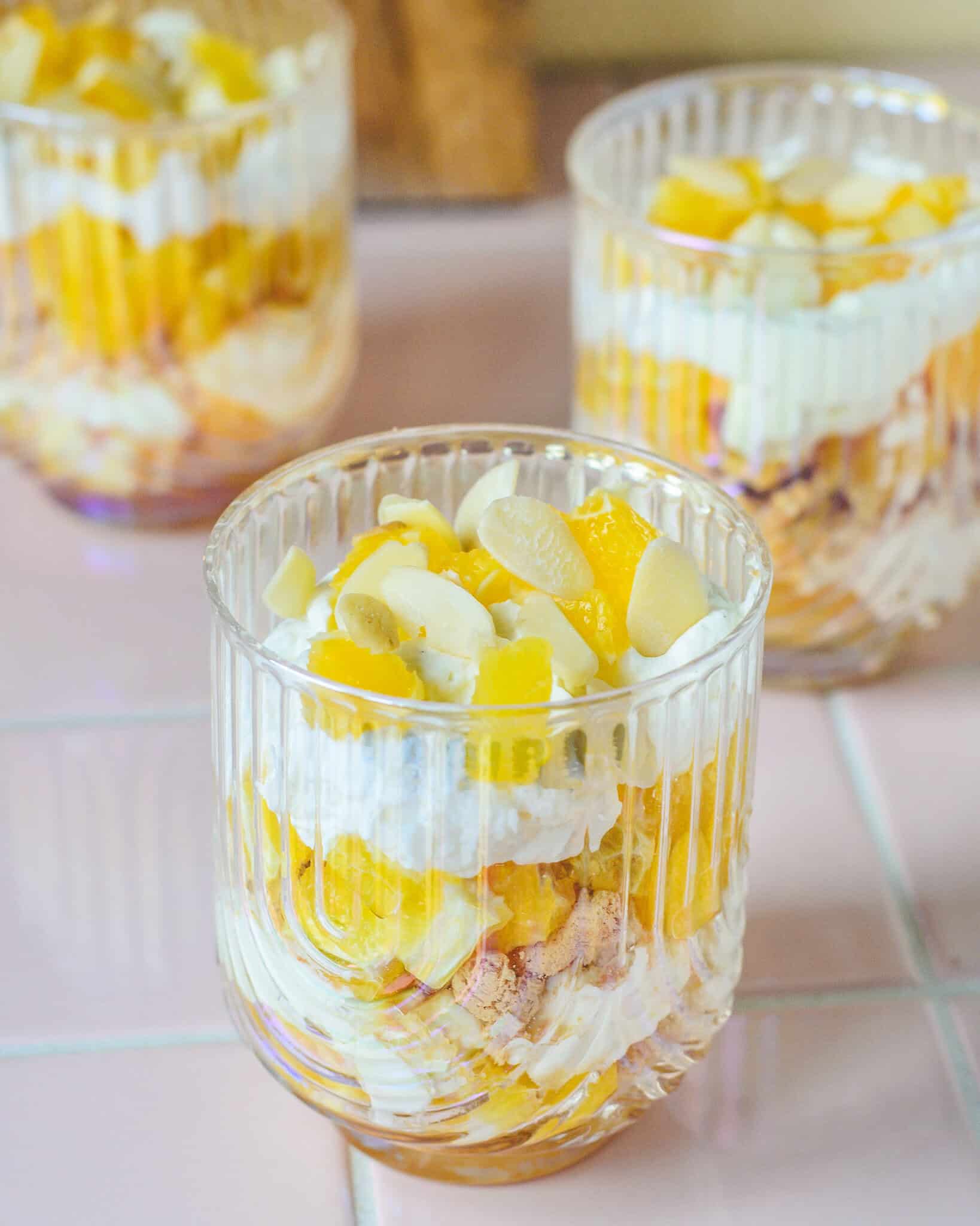 Appelsintrifli med mascarponecreme, friske appelsinstykker, sprøde makroner og ristede mandelflager serveret i glas – nem og lækker dessertopskrift.