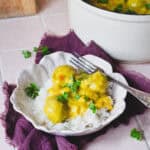 Hjemmelavede boller i karry med æble og grøntsager, anrettet med ris og persille i en dyb skål – klassisk dansk comfort food.