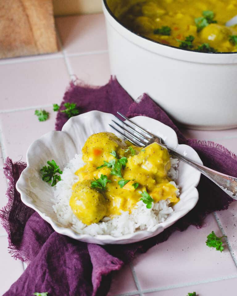 Hjemmelavede boller i karry med æble og grøntsager, anrettet med ris og persille i en dyb skål – klassisk dansk comfort food.