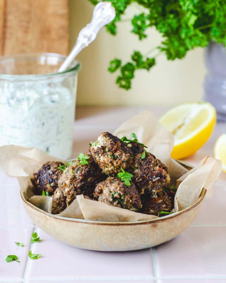 Saftige græske kødboller med feta, persille og soltørrede tomater serveret med tzatziki og citron.