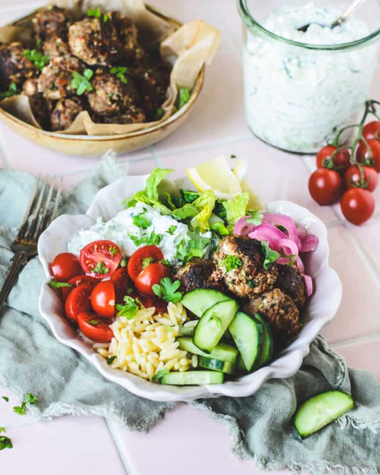 Græsk bowl med hjemmelavede kødboller, cremet tzatziki og orzo serveret med friske grøntsager og citron.
