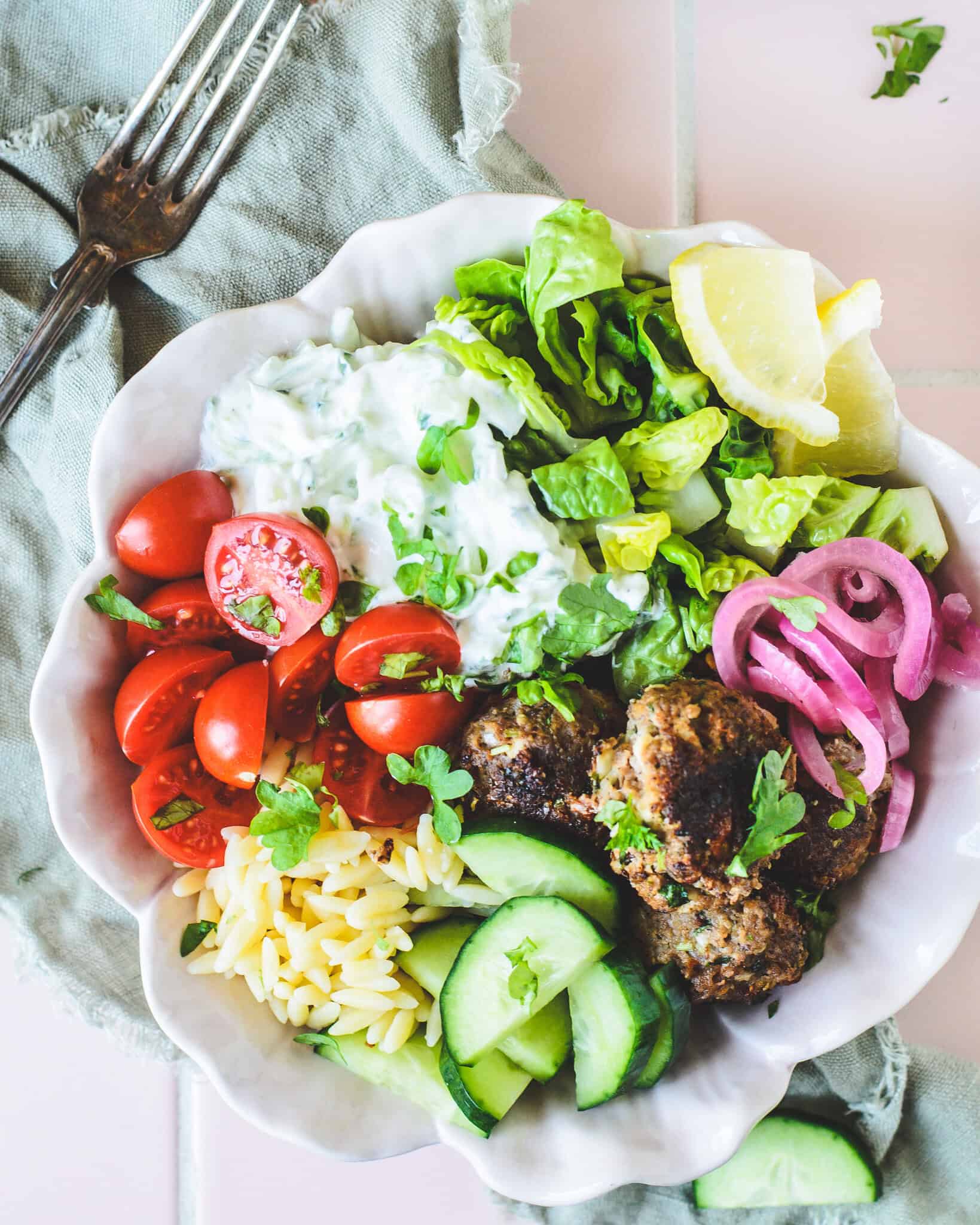 Farverig græsk bowl med kødboller, hjemmelavet tzatziki, hjertesalat, orzo og syltede rødløg.