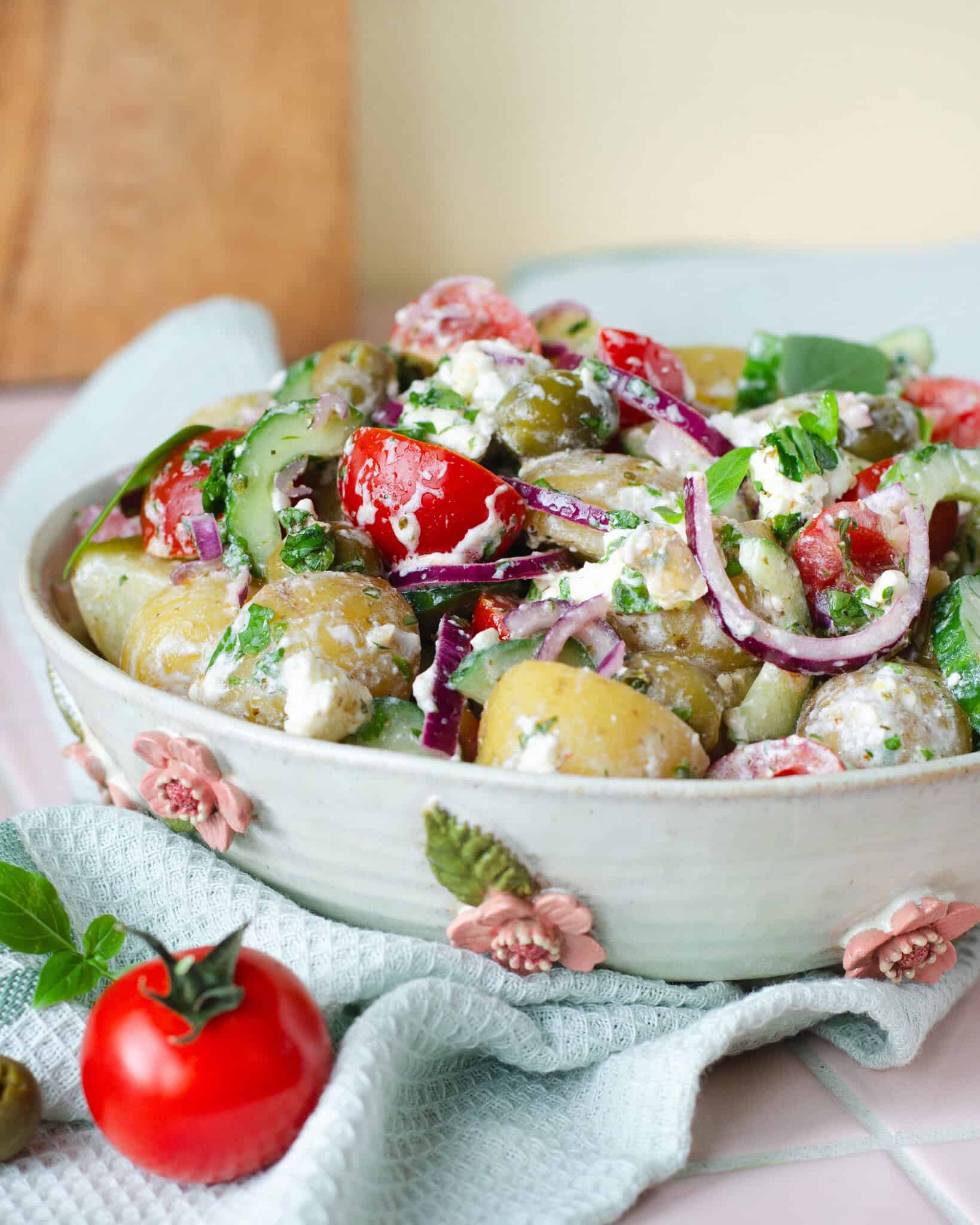 Græsk kartoffelsalat med feta, oliven, agurk, cherrytomater og rødløg serveret i en hånddrejet keramikskål.