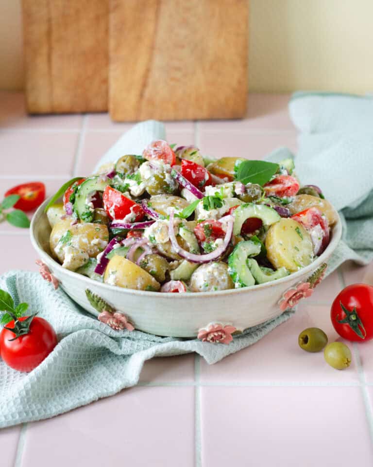 Græsk kartoffelsalat med feta, citron, oliven og friske grøntsager i en håndlavet keramikskål.