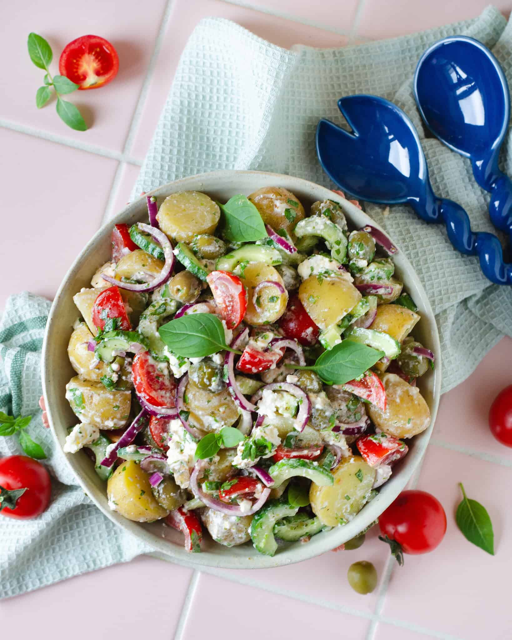 Græsk kartoffelsalat med feta, oliven, agurk og tomater fotograferet ovenfra i en hånddrejet keramikskål.